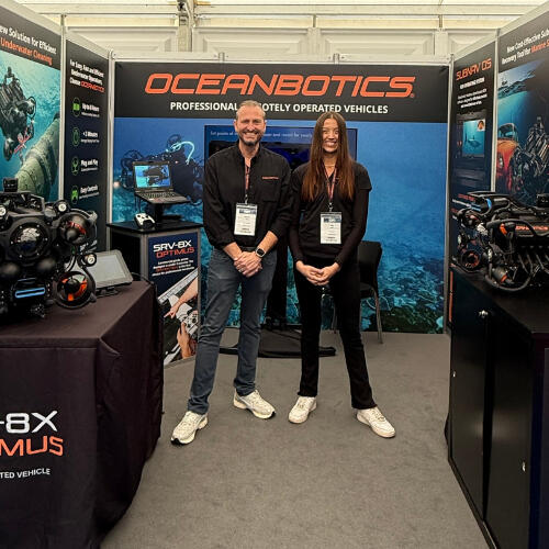 Two people standing in a booth for Oceanbotics underwater drones