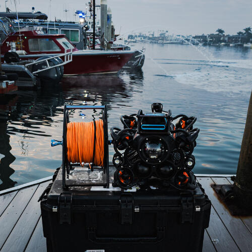 Underwater drone sitting on top of a case on a dock next to a police boat spewing water
