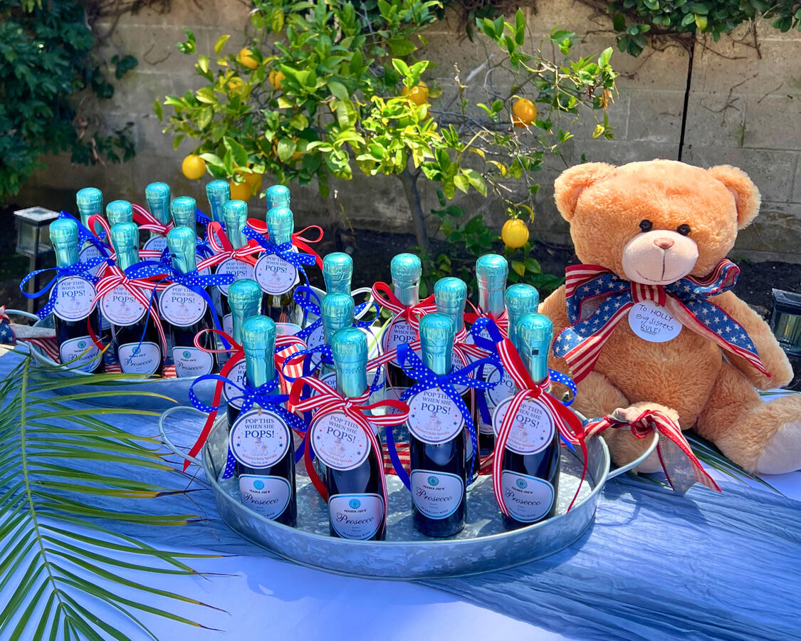 Prosecco bottle party favors with red white and blue ribbon and teddy bear for baby shower, Orange County event design